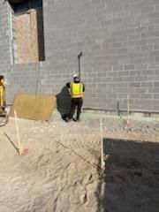 Construction worker with safety vest using surveying equipment near a concrete block wall and stakes.