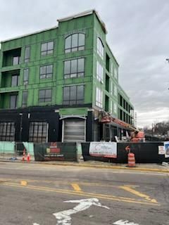 Building under construction with green siding and construction barriers on street.