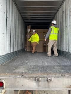 Two workers in safety vests and hard hats inside a semi-truck trailer loading boxes.