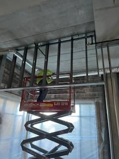 Worker on a lift constructing a metal frame ceiling inside a building.
