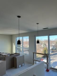 Two black pendant lights hang in a room with large windows, near construction materials.