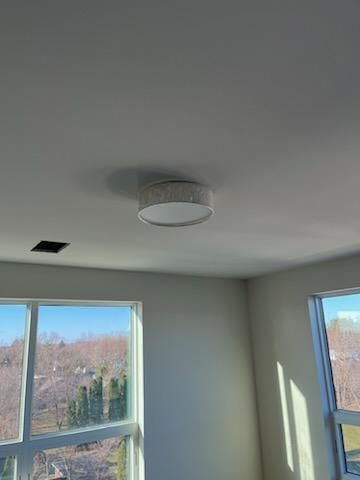 Flush-mount ceiling light fixture in a room with windows and a dark vent on the ceiling.