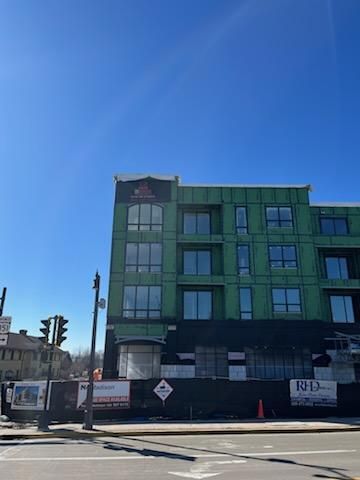 Construction site of a multi-story building, exterior view. Green siding, blue sky, street, traffic light.