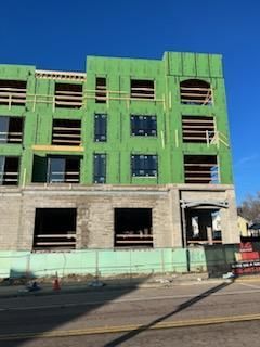 Building under construction, with green sheathing, windows, and scaffolding. A clear blue sky is visible.