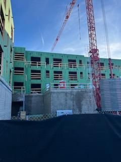 Construction site with a red crane and a building framed in green with open windows against a blue sky.