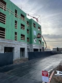 Building under construction, green sheathing, crane, cherry picker, overcast sky.