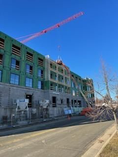 Building under construction, crane overhead; exterior view, blue sky.