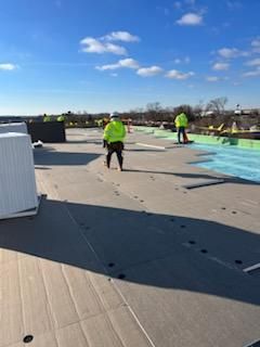 Workers in yellow vests installing roofing on a sunny day.