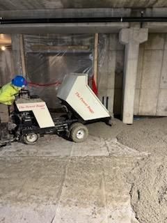 Worker operating a concrete buggy, dumping load onto concrete floor in a construction setting.