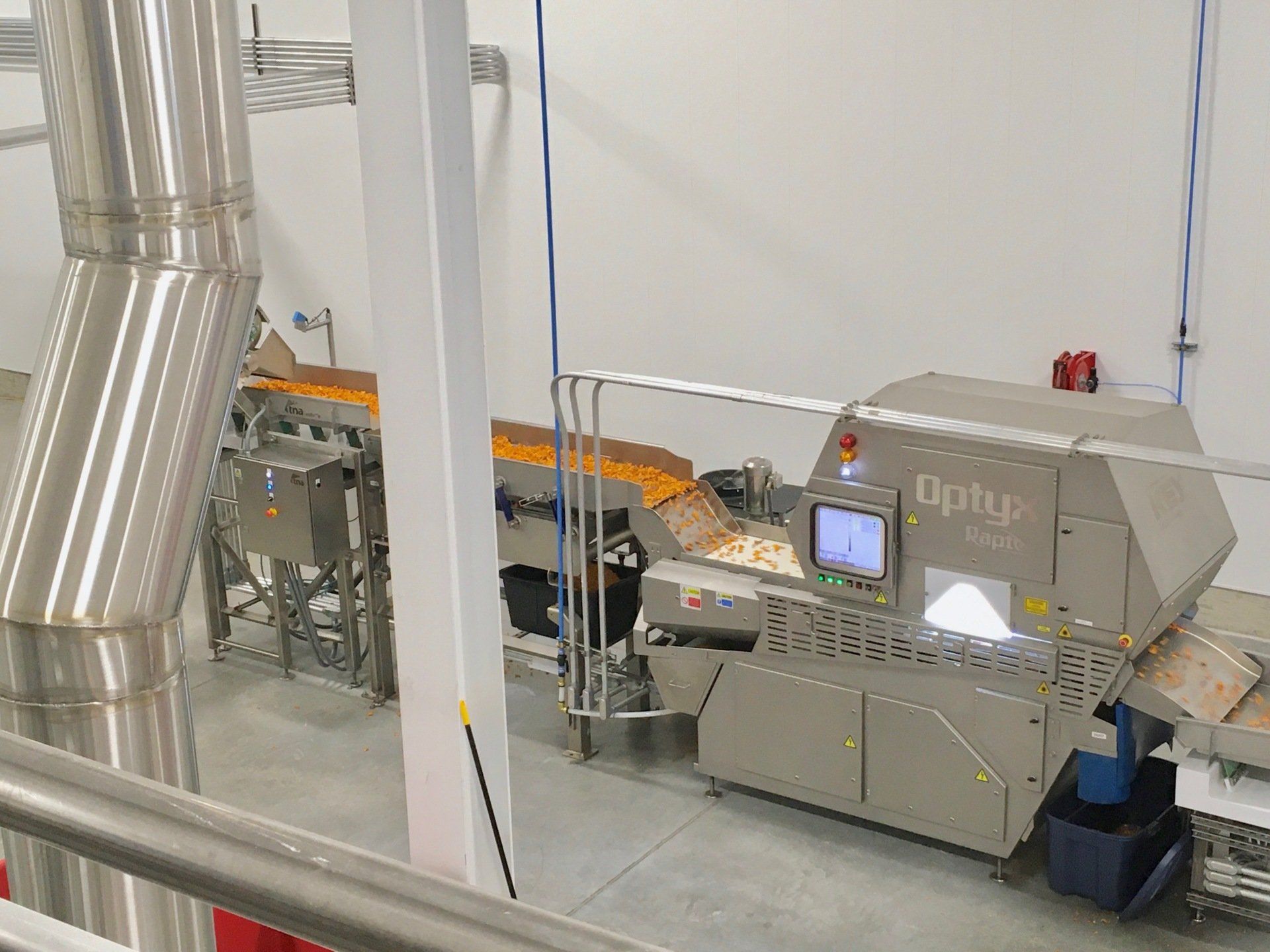 Industrial food processing equipment in a factory setting, with conveyor belts and stainless steel machinery.