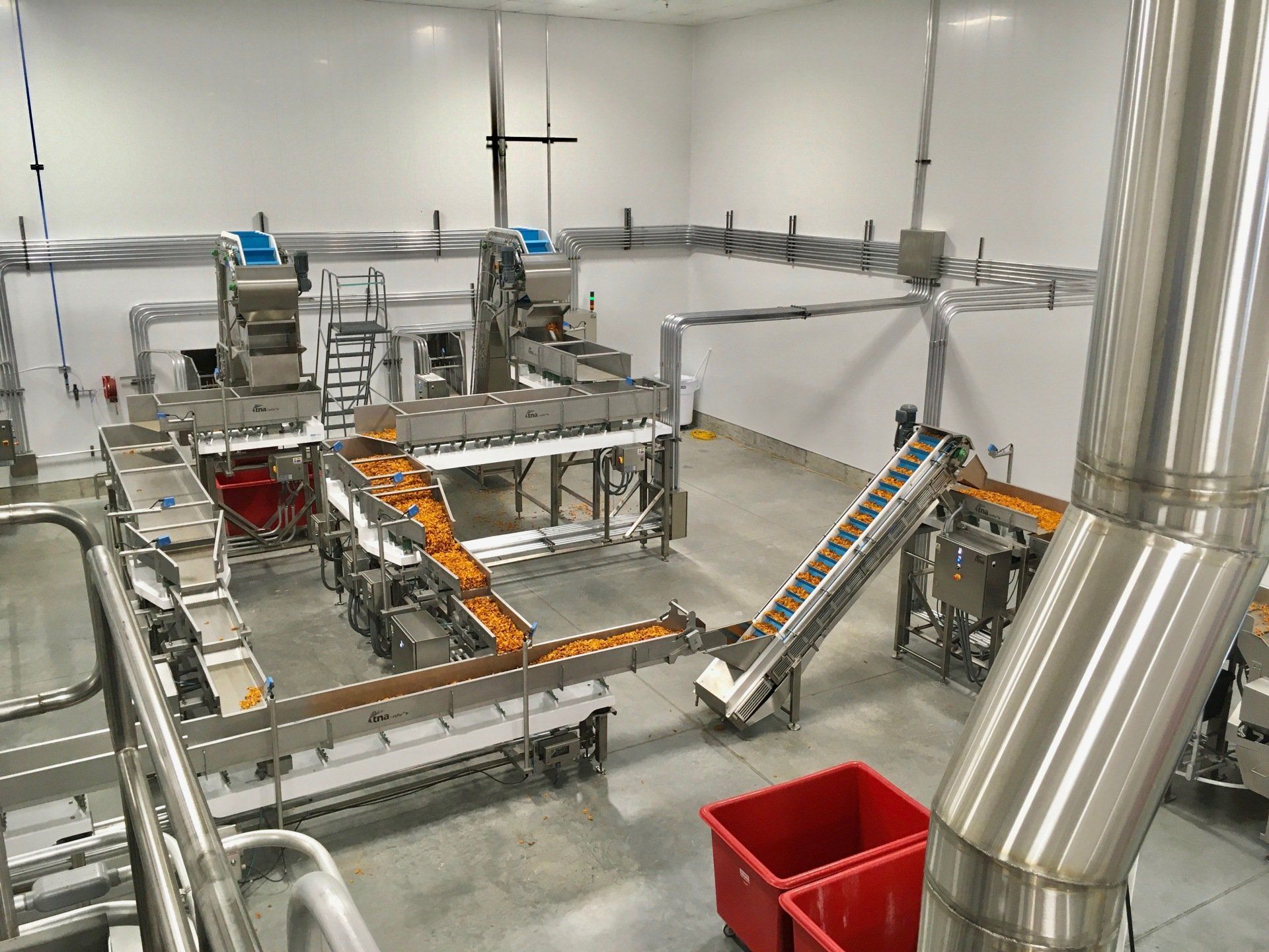 Food processing facility with stainless steel machinery and conveyors, transporting product.