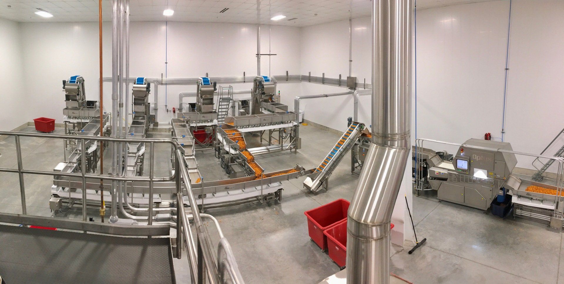 Processing facility: stainless steel machinery, conveyor belts, and a worker in a large, white room.