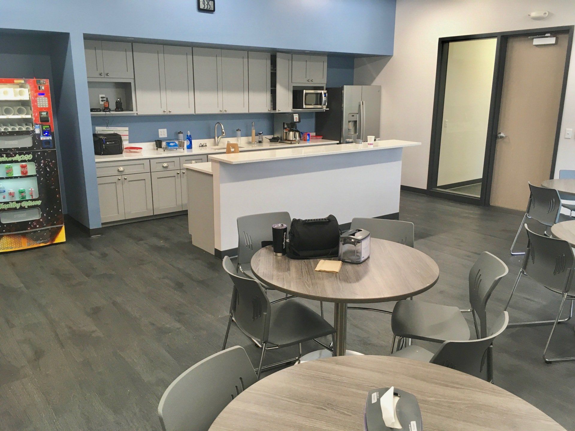 Break room with a kitchen and round tables with chairs. Vending machine on left.