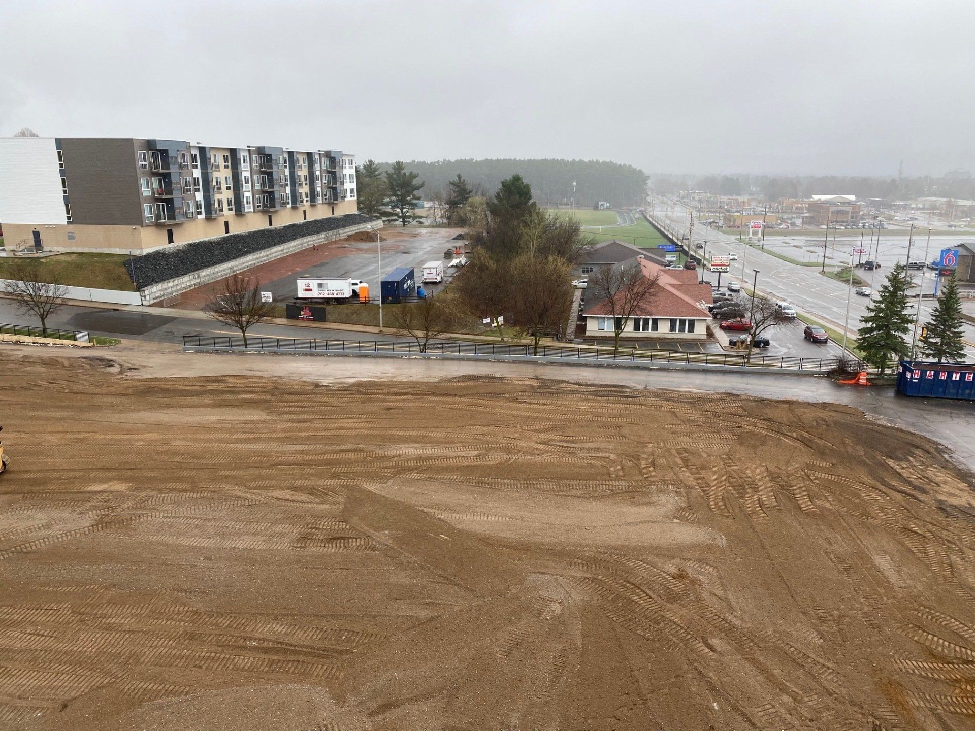 View of a construction site with dirt, buildings, and a road under a gray sky.