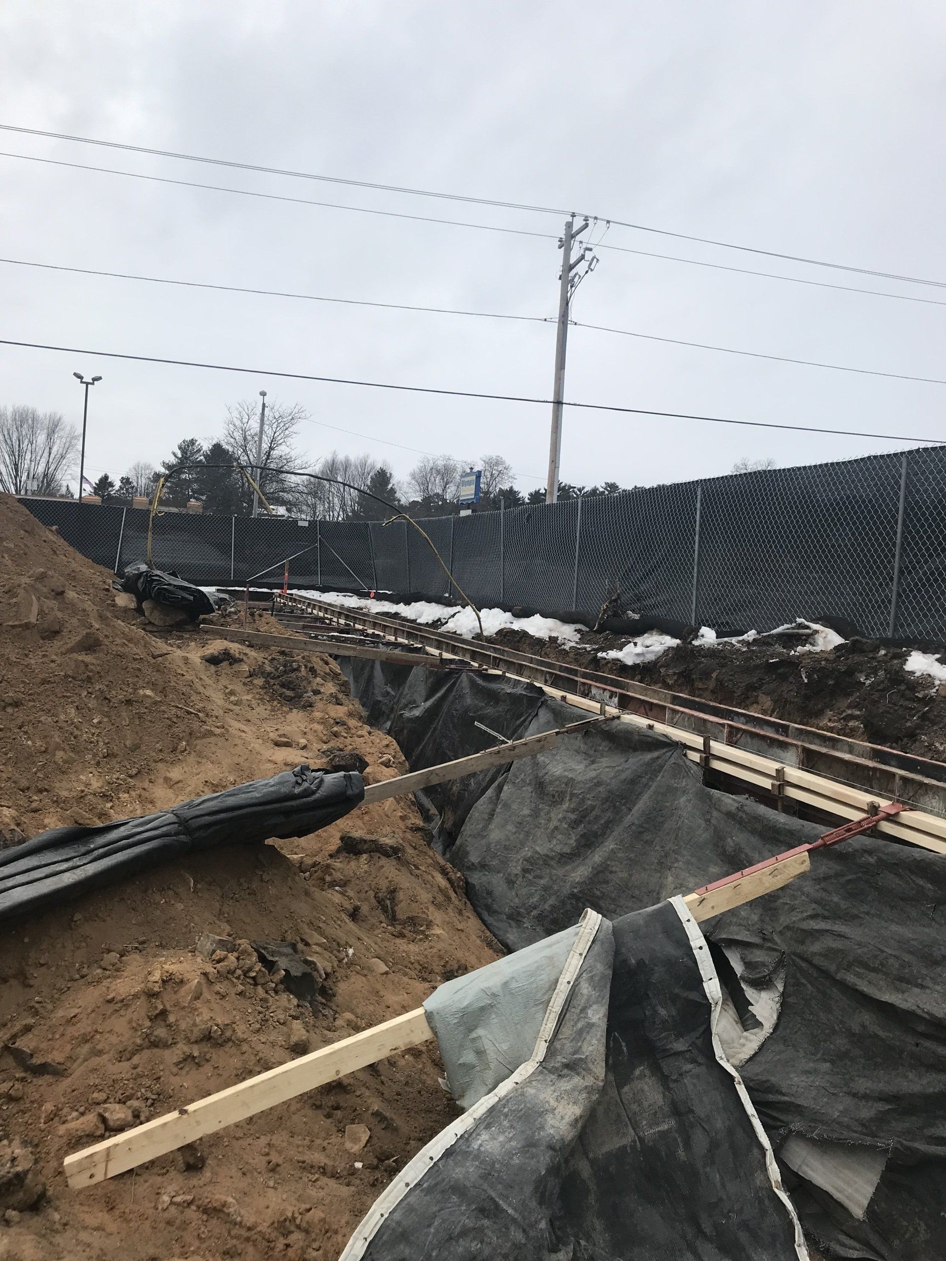 Construction site with dirt, black tarps, wood, and a mesh fence.