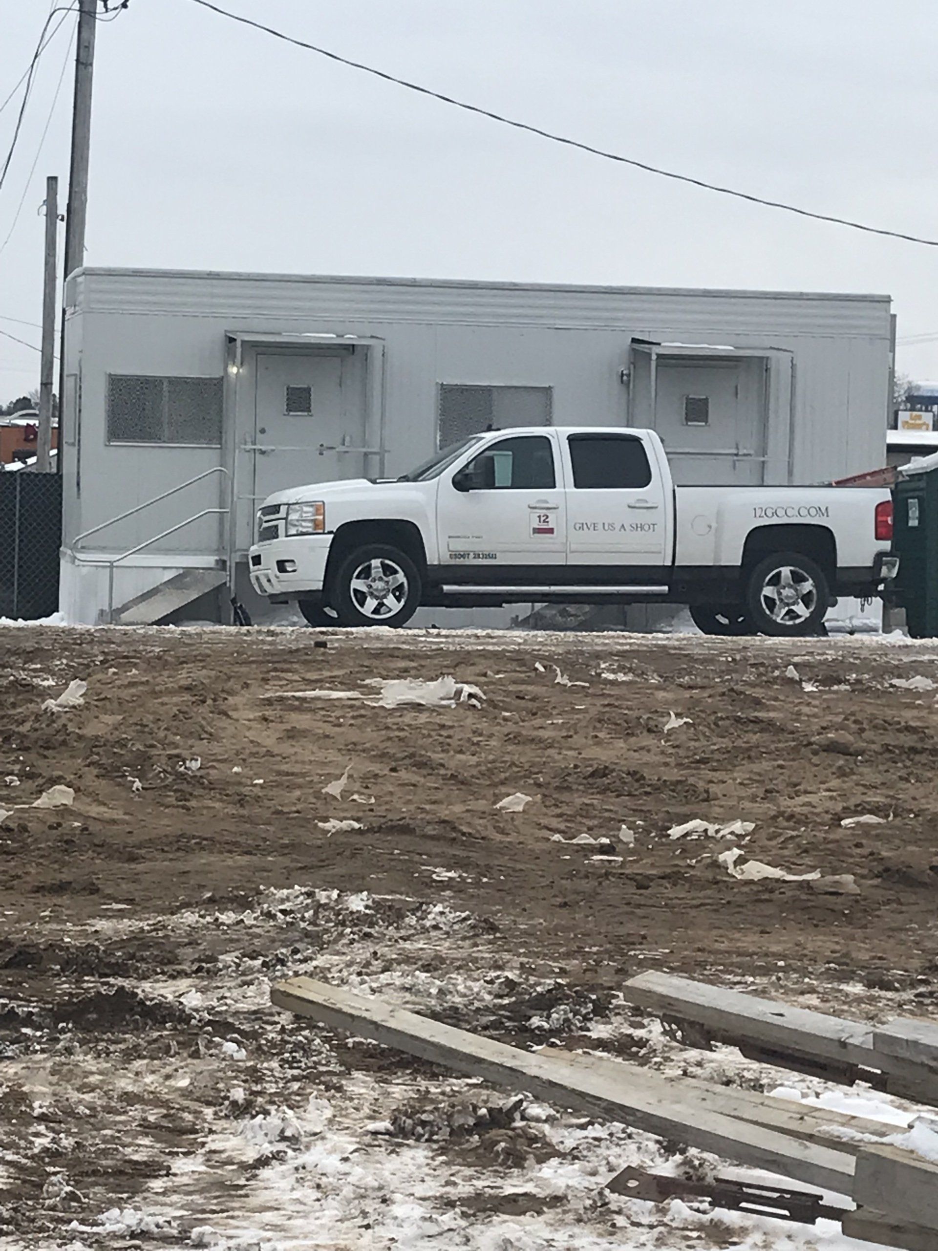 White truck parked next to a rectangular building on a construction site; overcast sky.