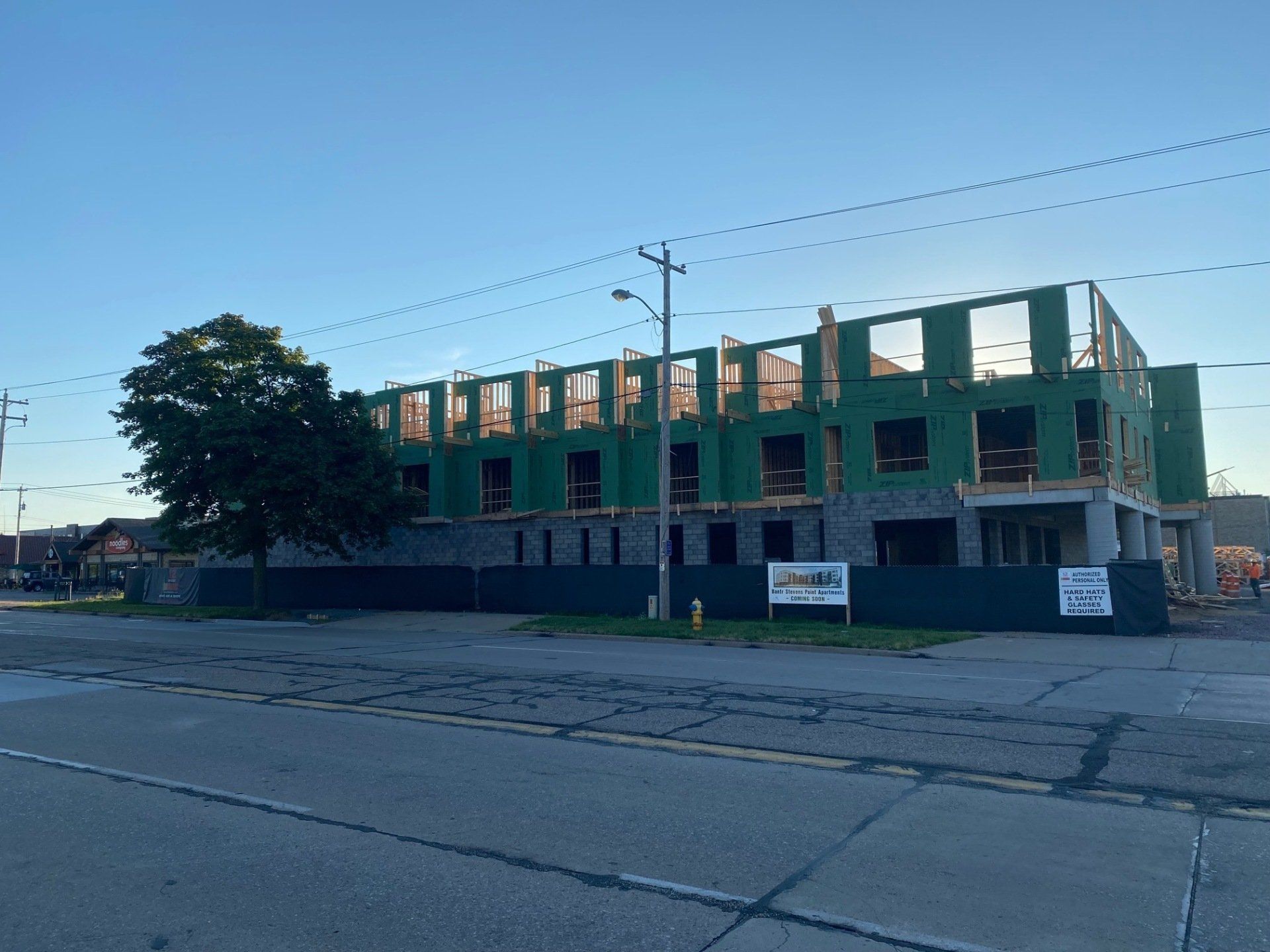 Building under construction with wooden frames and green sheathing behind a chain-link fence.