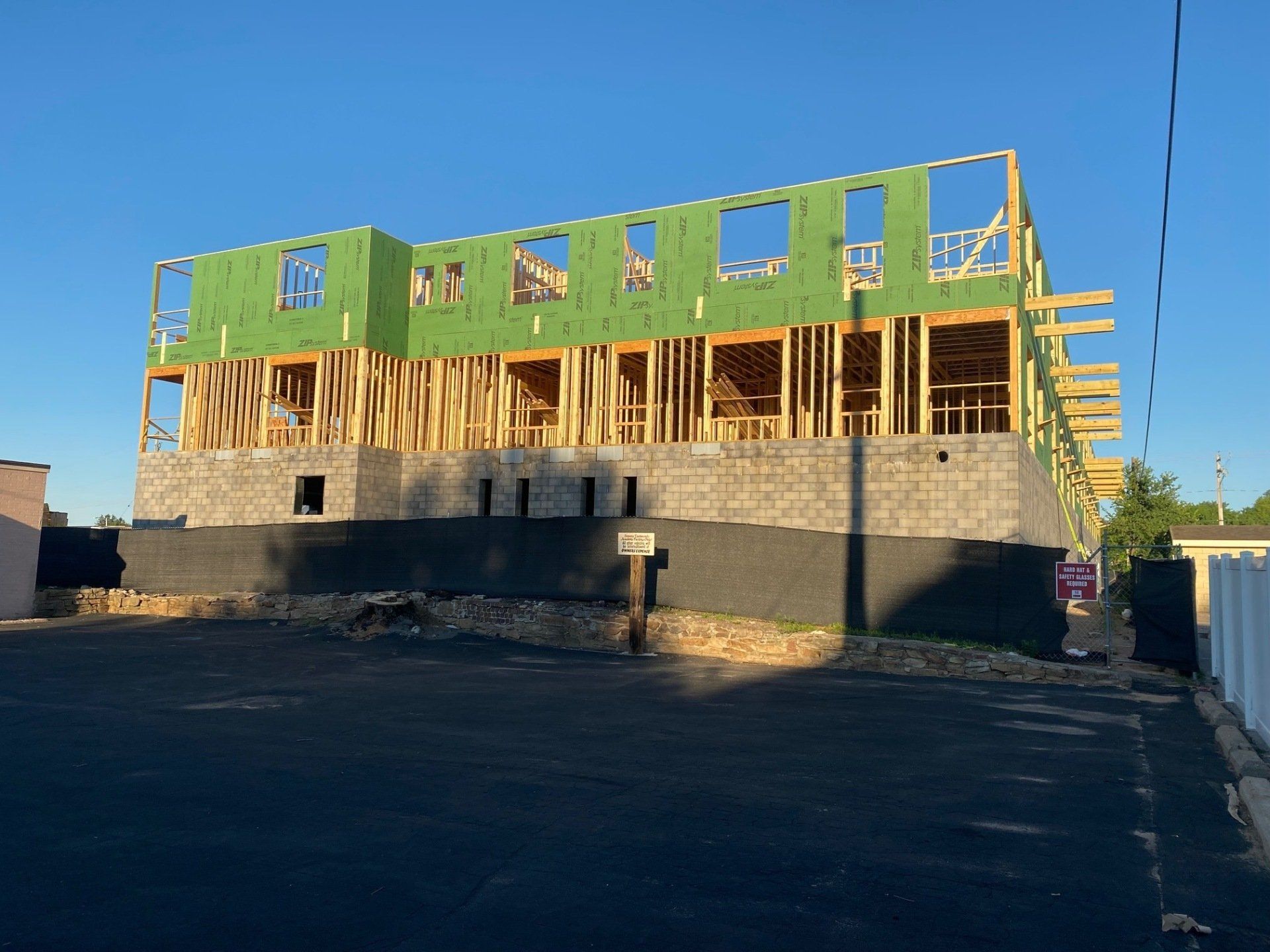Building under construction: wooden frame with green sheathing, on a stone base, against a blue sky.