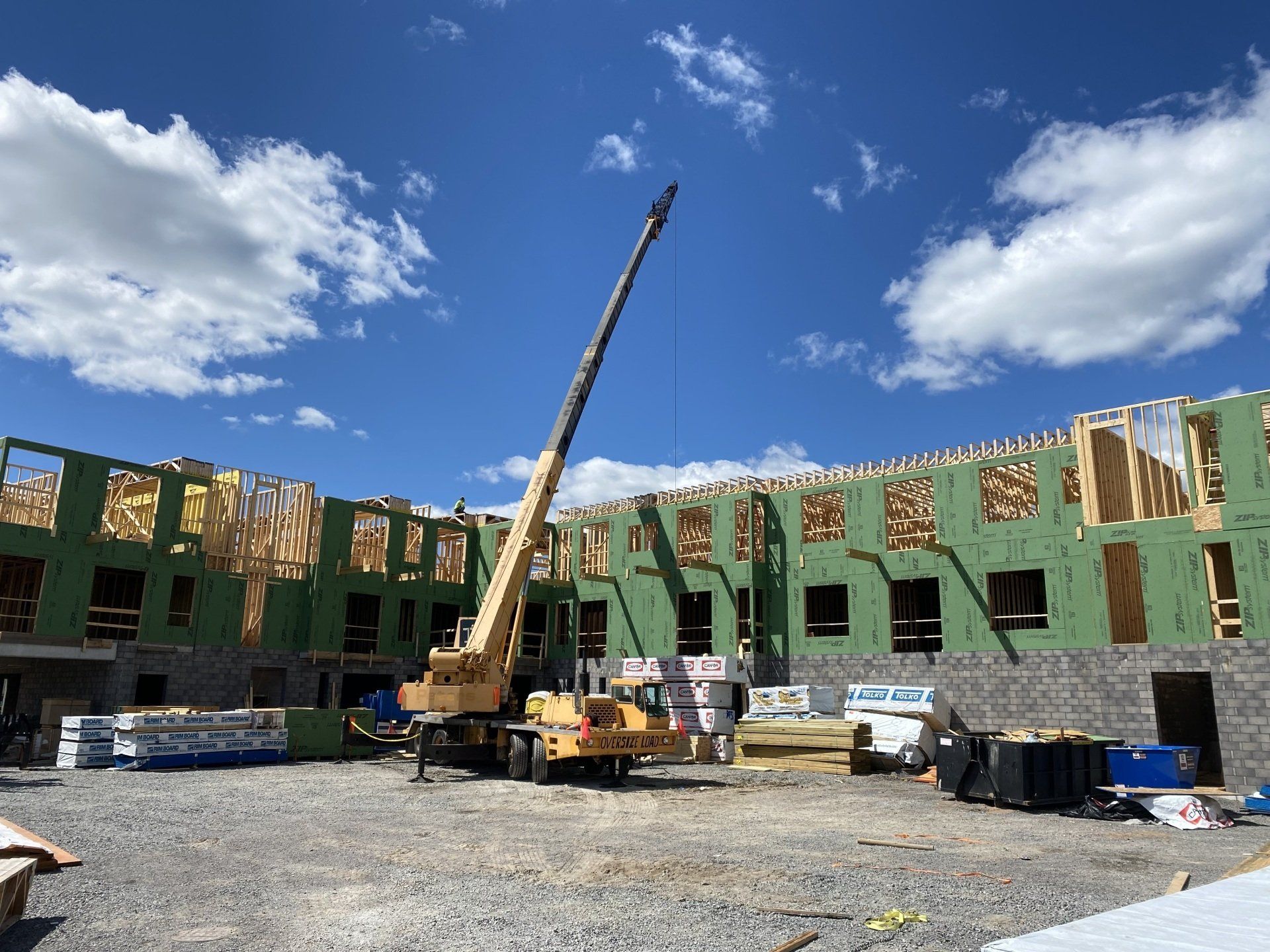 Construction site with crane lifting materials. Unfinished building with exposed framing, blue sky.