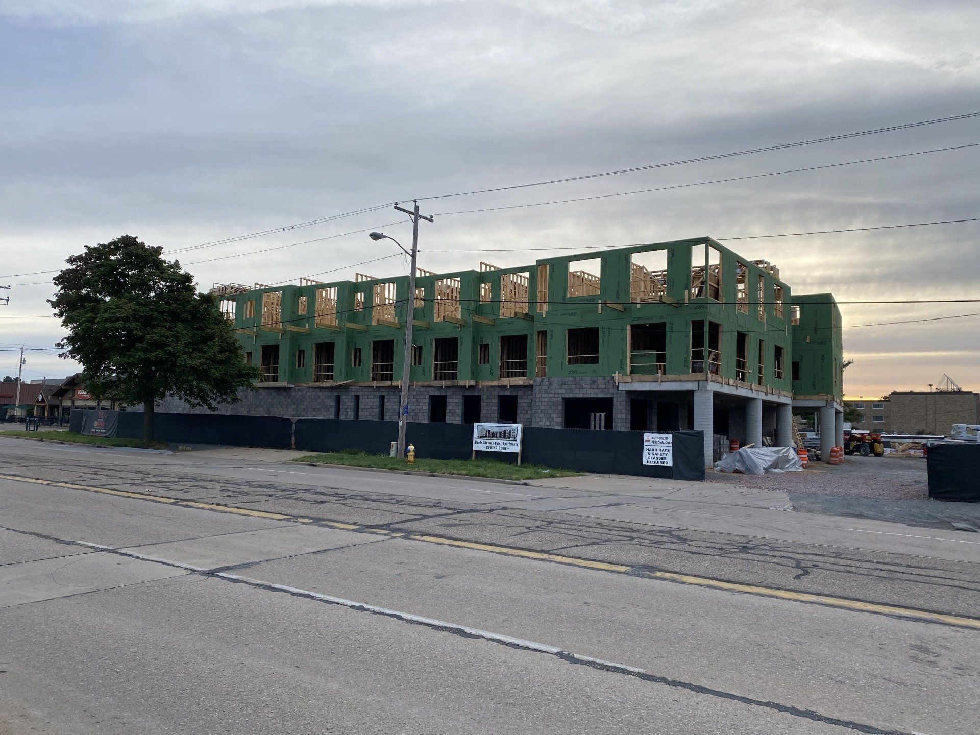 Construction site of a multi-story building frame, gray, green, and tan colors, under a cloudy sky.