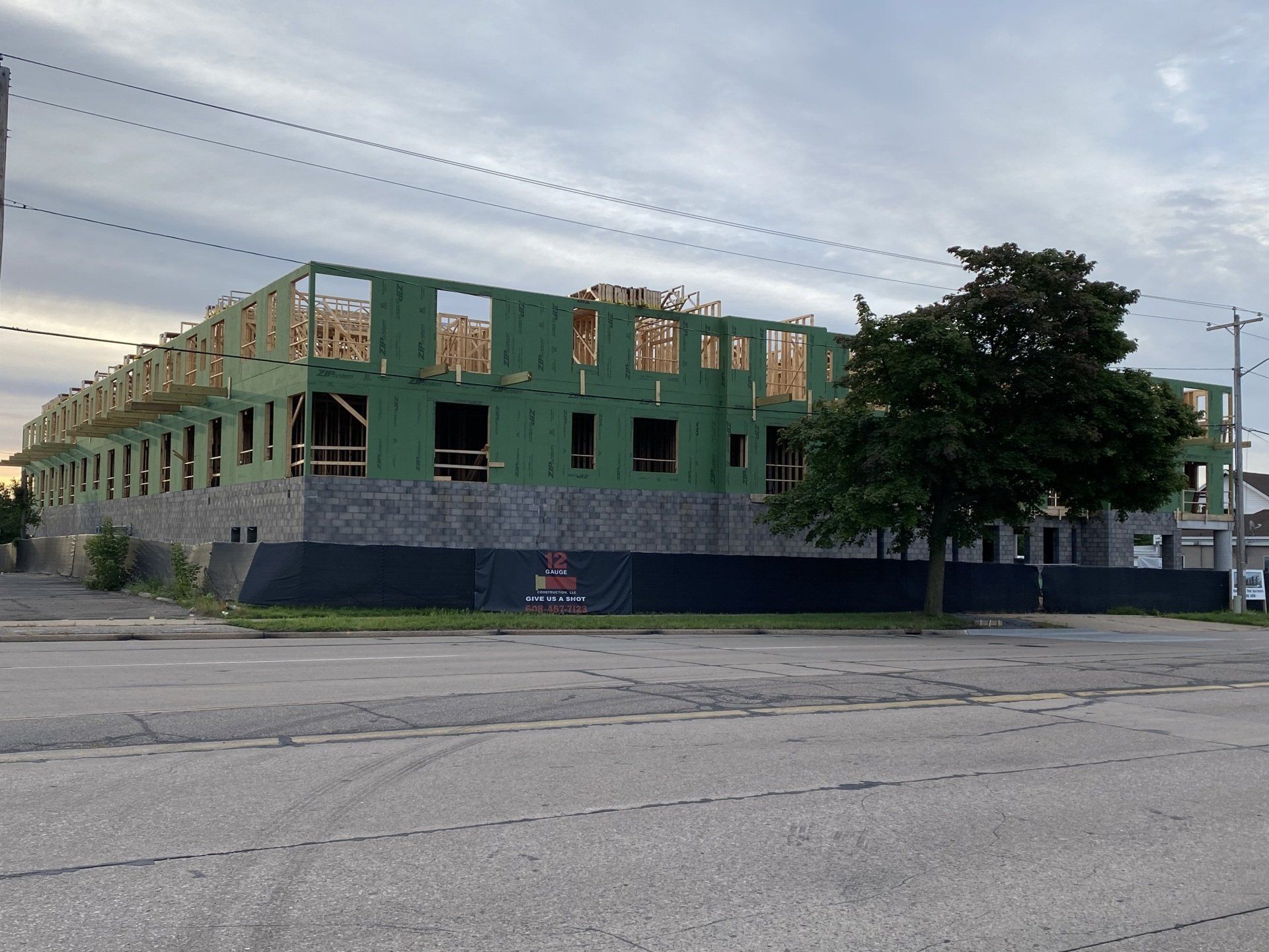 Building under construction; wood framing and green sheathing. Black fence in front of unfinished structure.