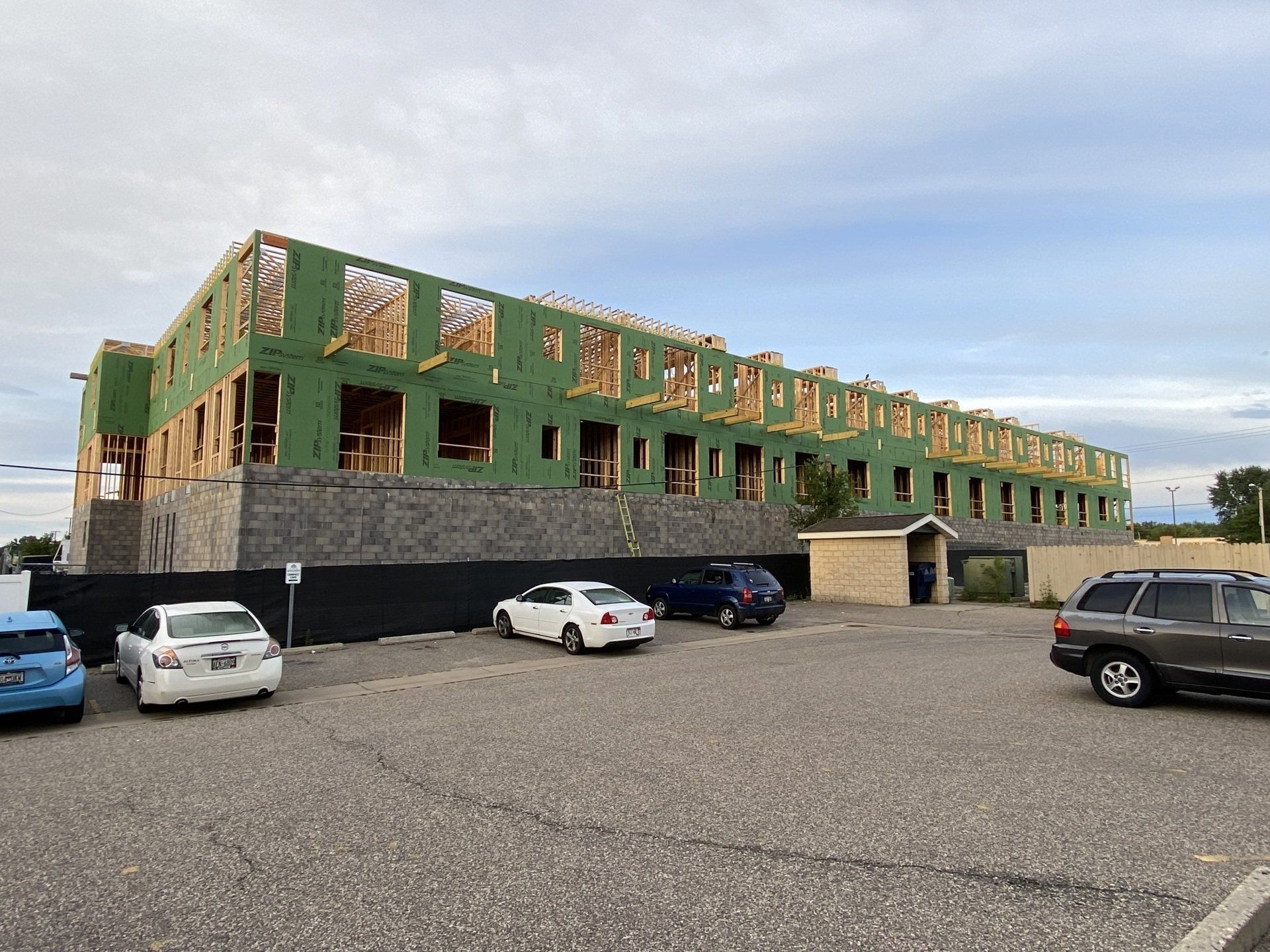 Building under construction with wood framing and cars parked in front.