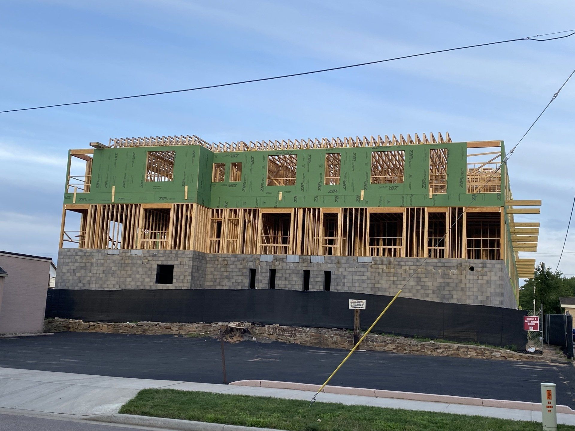 Multi-story building under construction; wooden framing, stone base, black tarp, and blue sky.