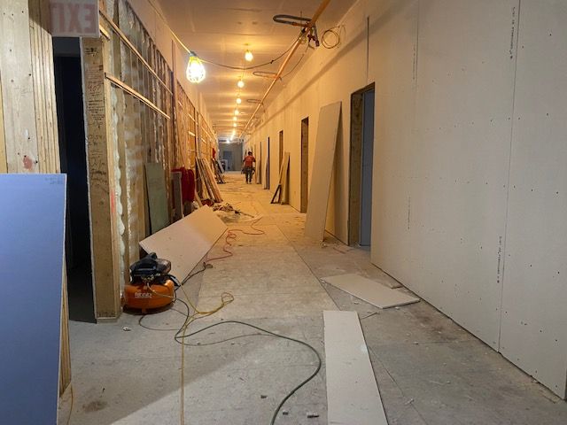 Hallway under construction with drywall and tools. One person walking toward the far end.