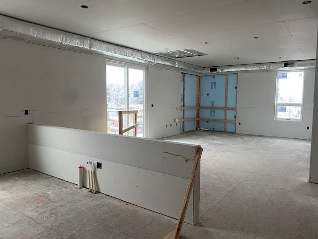 Interior of a room under construction, with drywall, windows, and exposed ductwork.
