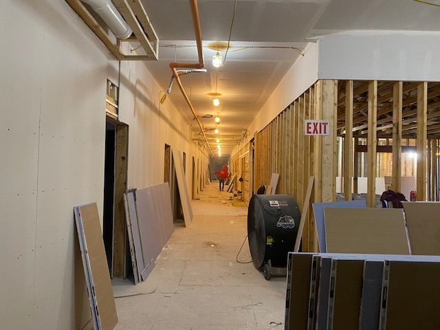 Hallway under construction with exposed wood framing, drywall, and a fan.