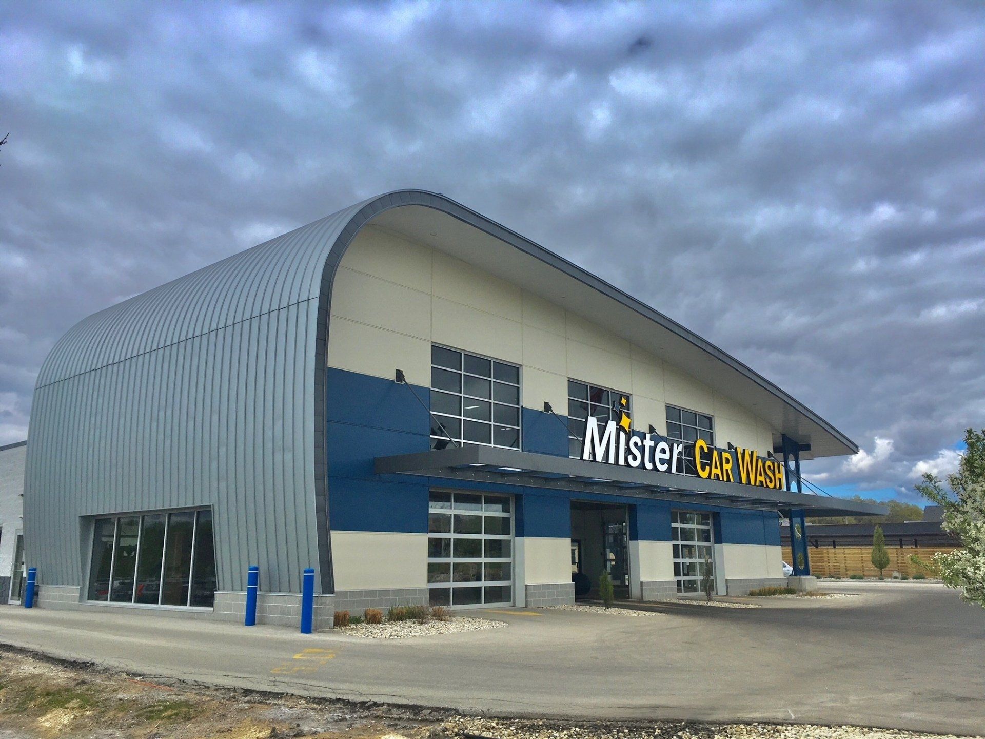 Mister Car Wash exterior with blue and gray facade, arched roof, glass garage doors under cloudy sky.