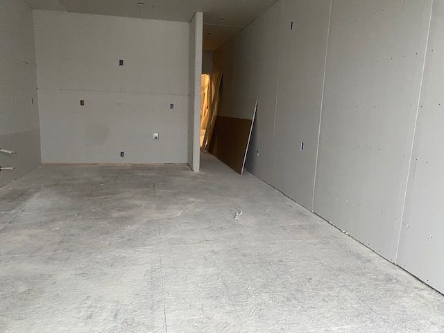 Empty room with concrete floor and drywall walls under construction.