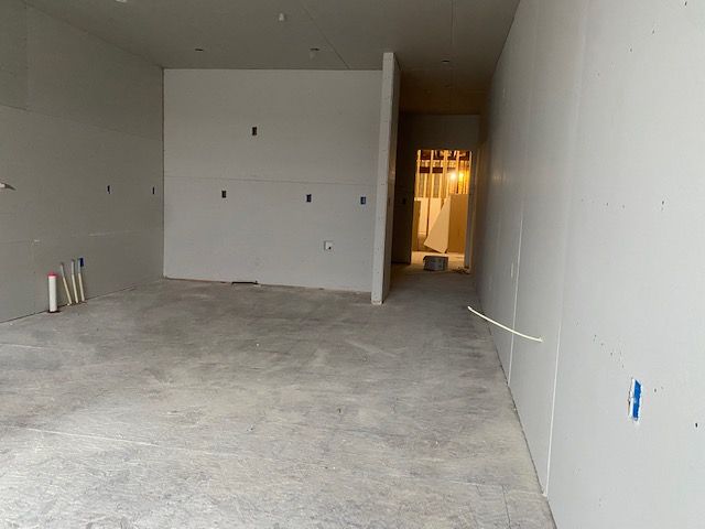 Interior of a room under construction, with drywall walls and concrete floor. Hallway in the background.