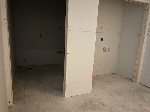 Unfinished room with drywall and concrete floor, showing two doorways and electrical outlets.