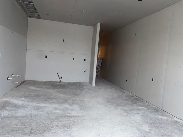Empty room under construction; drywall walls, concrete floor, electrical outlets, and plumbing visible.