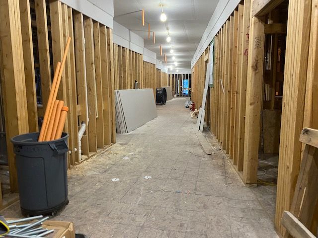 Hallway under construction; exposed wooden studs, drywall sheets, and electrical conduits visible.