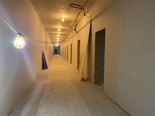 Long hallway under construction with drywall and bare light bulbs.