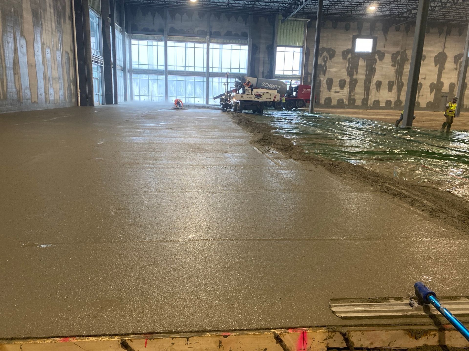 Newly poured concrete floor in a large industrial building, construction in progress.