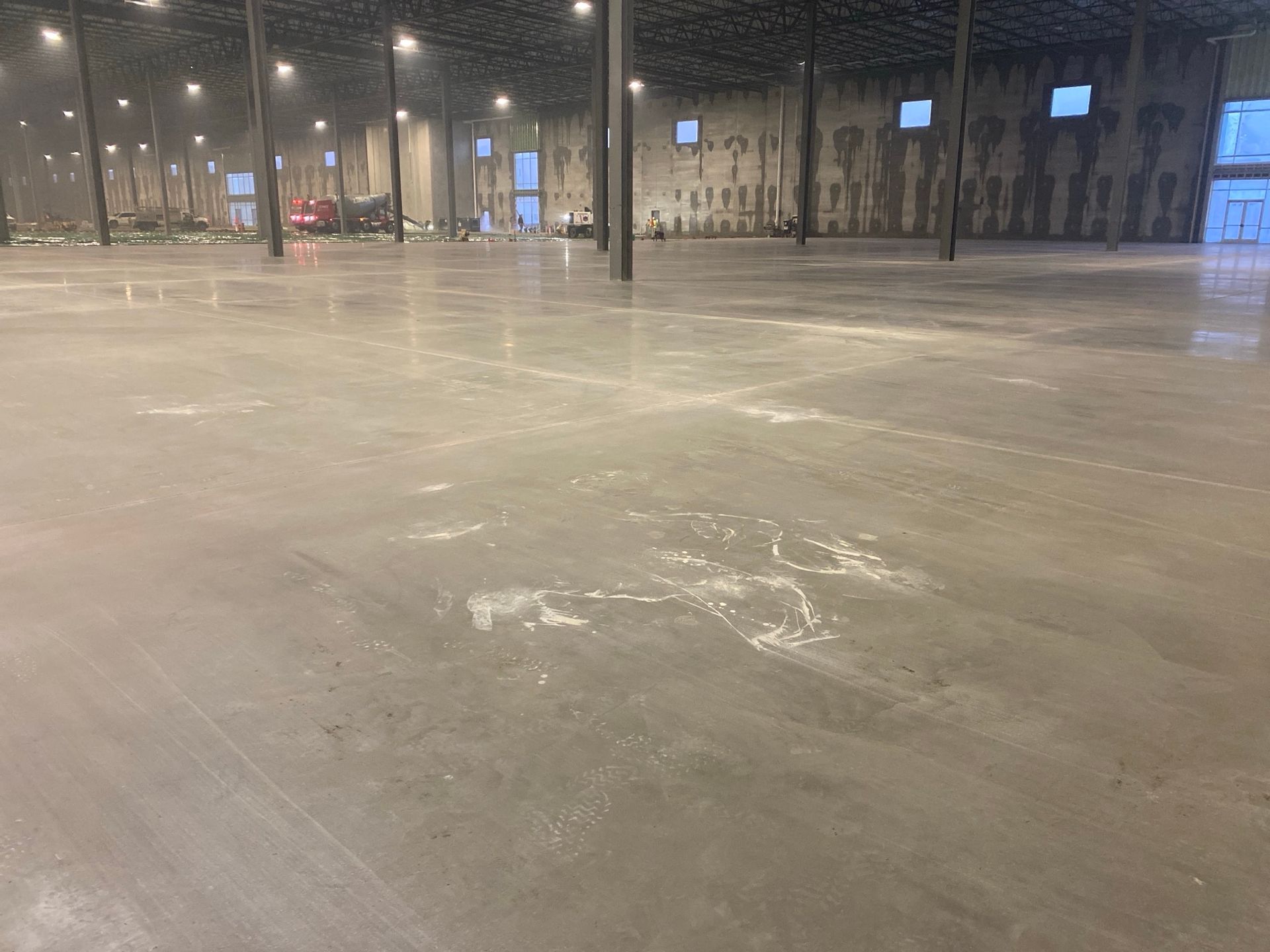 Large, empty concrete warehouse interior; visible support columns, exterior windows, and overhead lighting.
