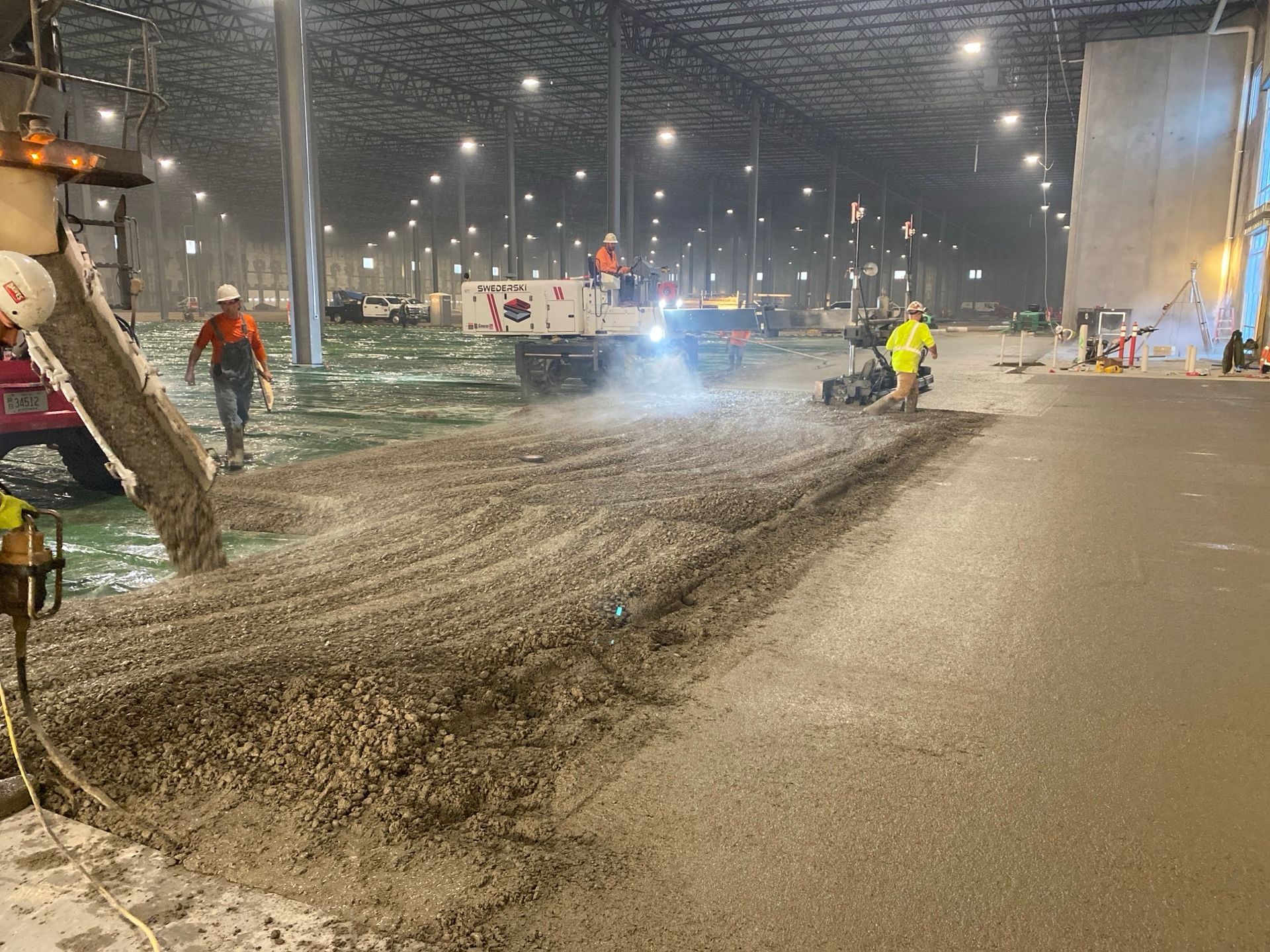Concrete being poured and smoothed inside a large building by construction workers.