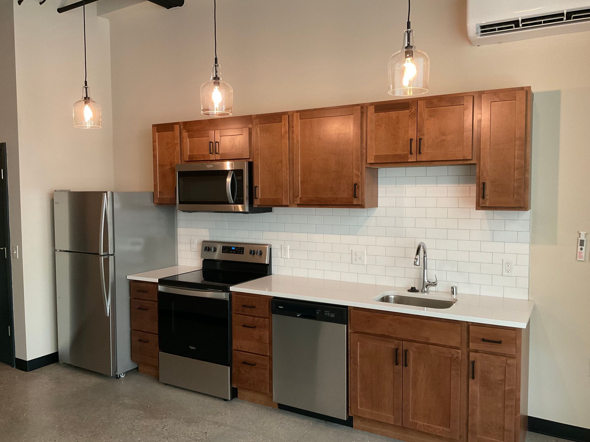Modern kitchen with stainless steel appliances, brown cabinets, white countertops, and subway tile backsplash.