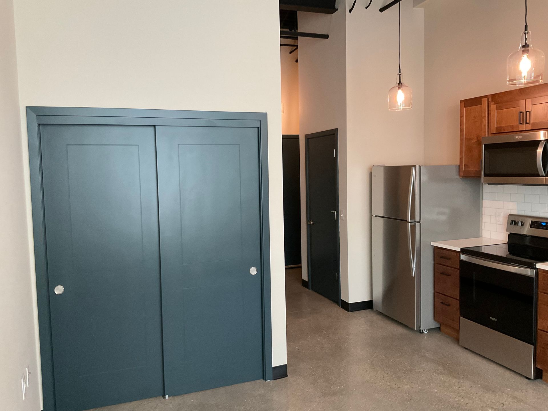 Kitchen and closet in a modern apartment; stainless steel appliances, dark blue closet doors, and wood cabinets.