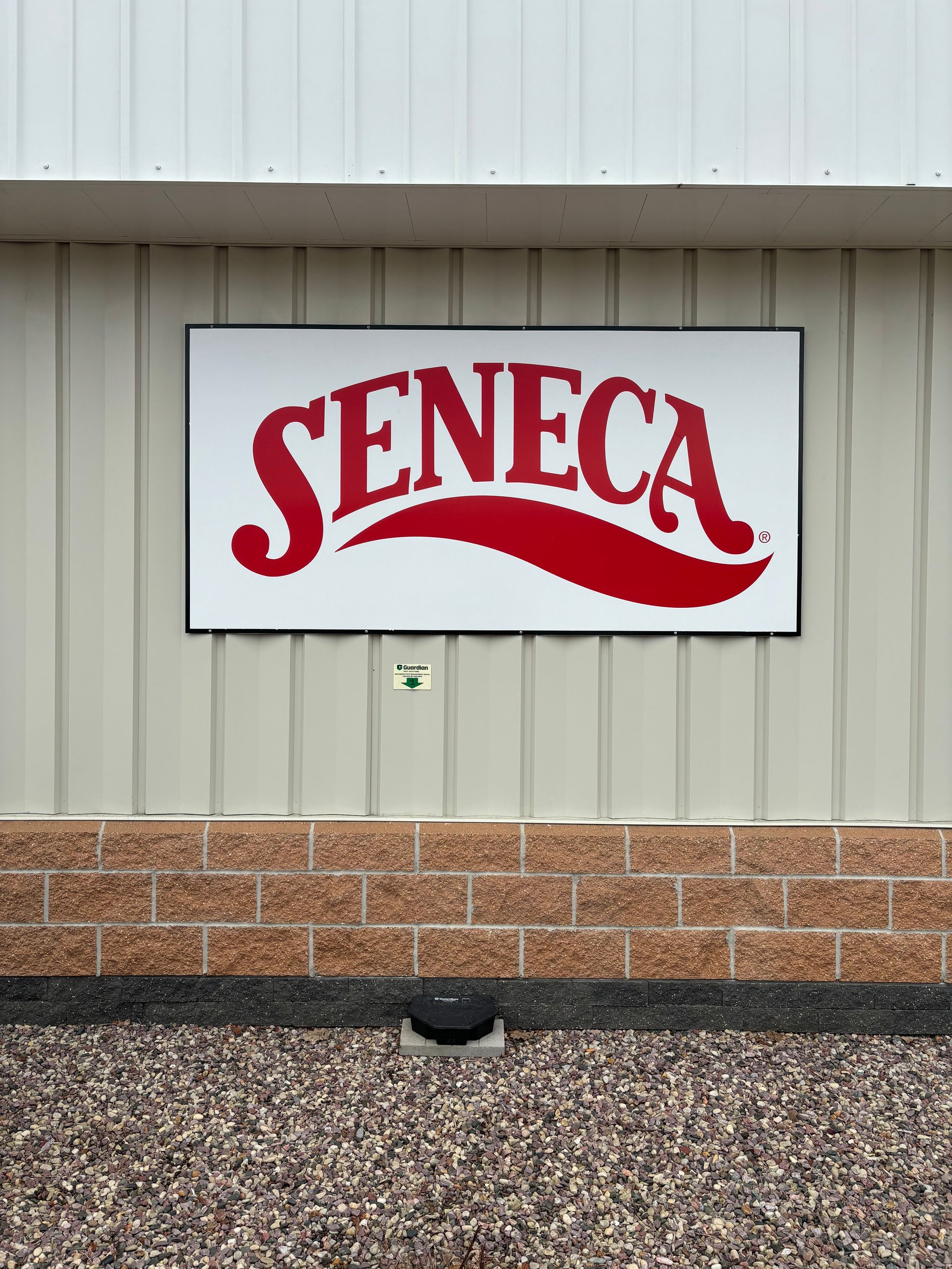 Sign for Seneca, red script on white background, mounted on a tan building.