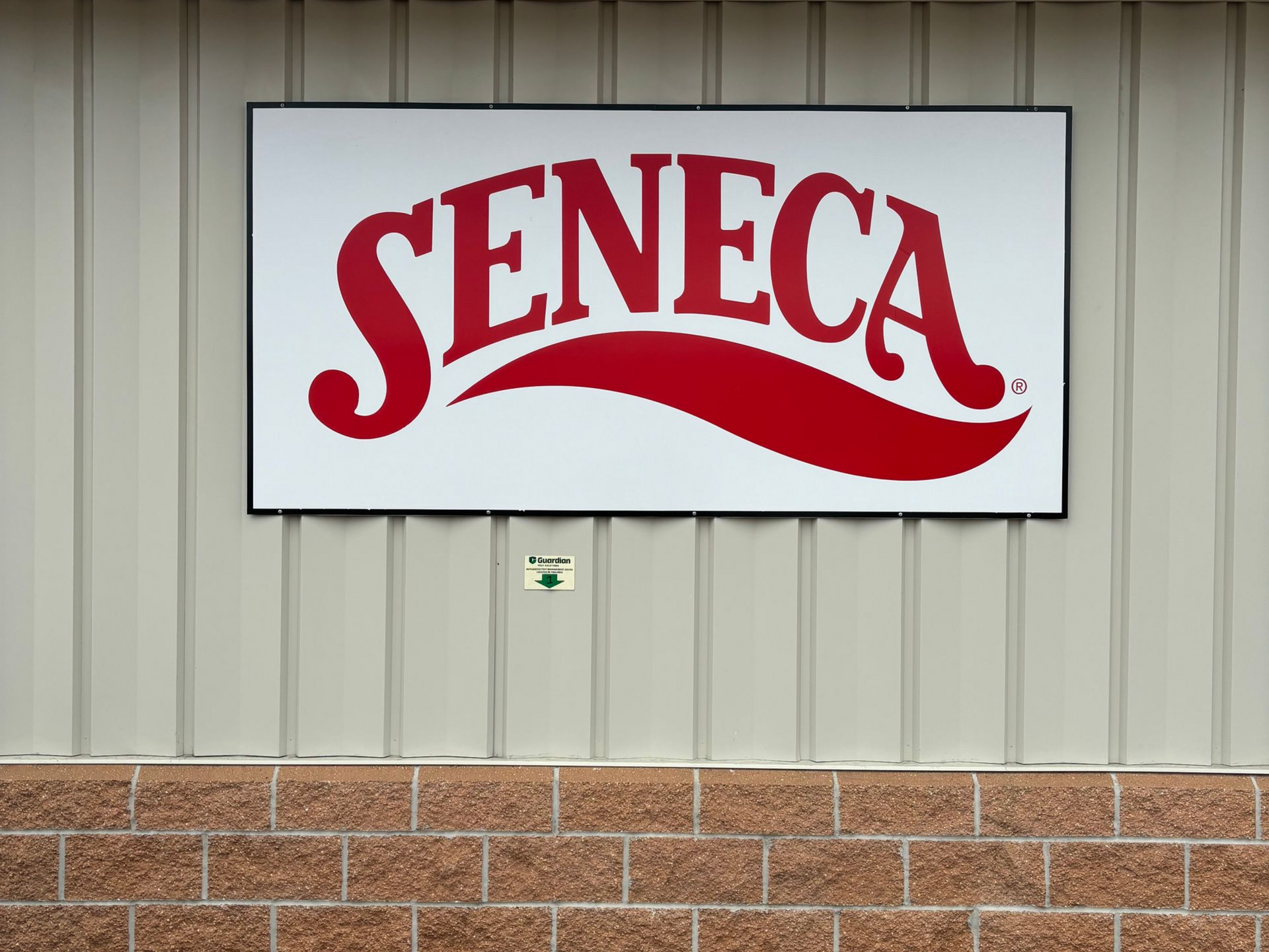 Sign for Seneca Foods, red lettering on white background, above a brick and siding facade.