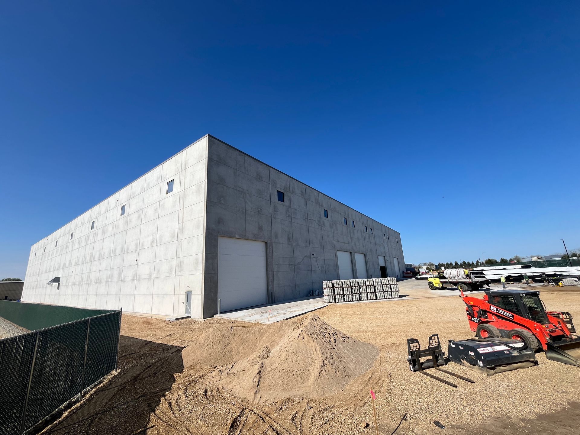 Large gray industrial building under construction; clear blue sky, construction equipment visible.