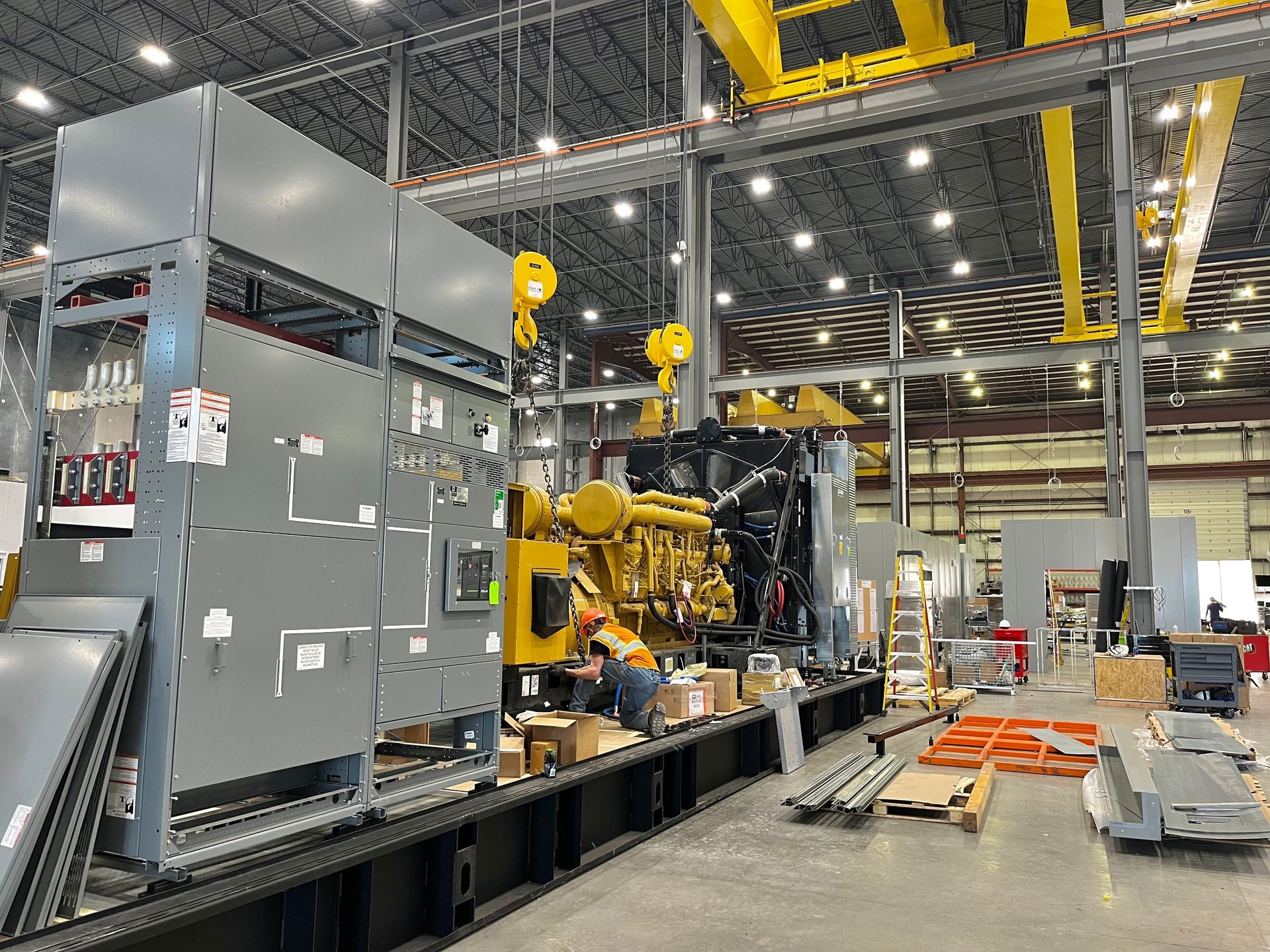 Factory assembly of large diesel generator, yellow and black, with workers.
