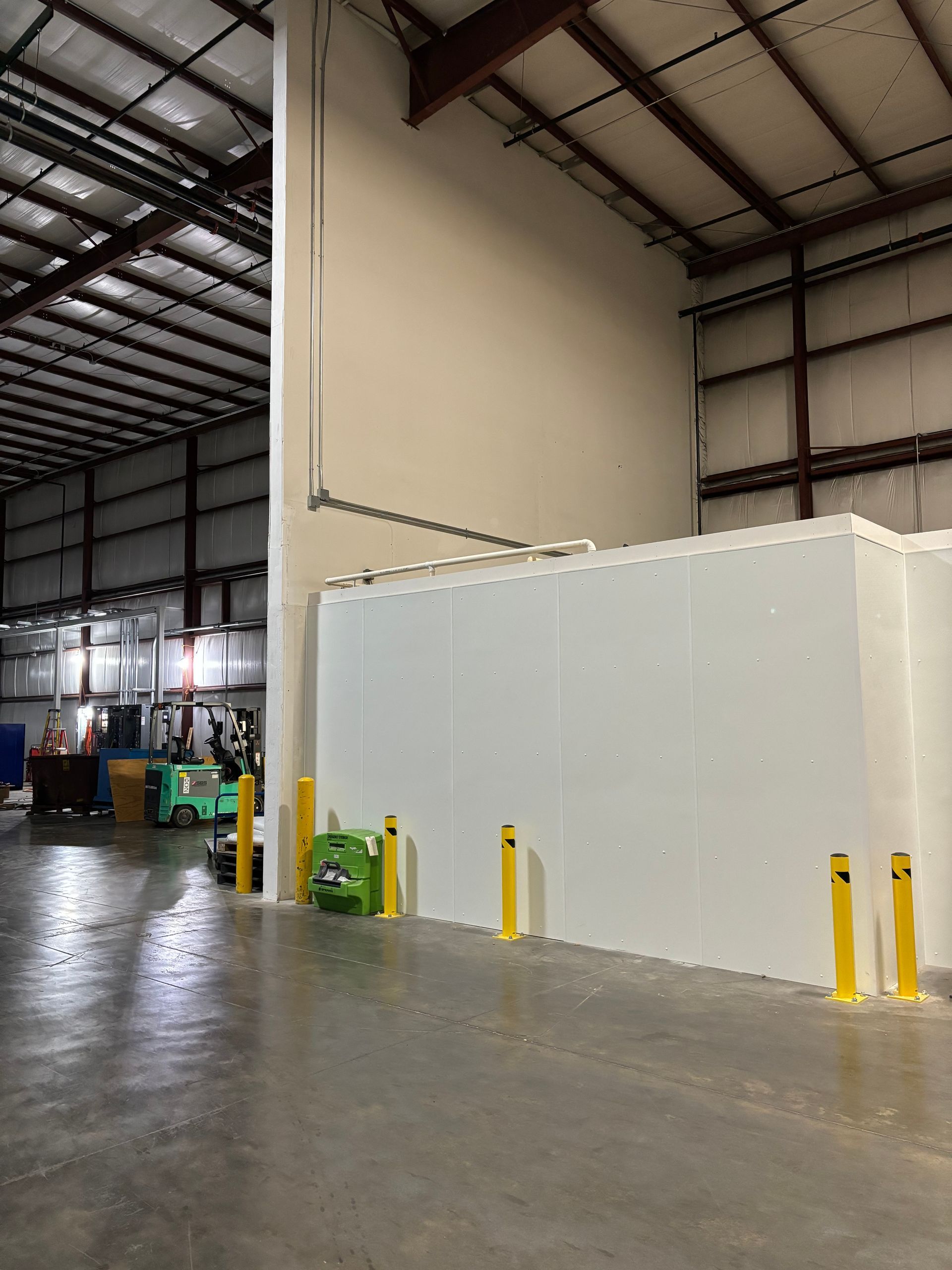 Warehouse interior with white walls, steel beams, and a concrete floor. Yellow bollards and equipment are present.