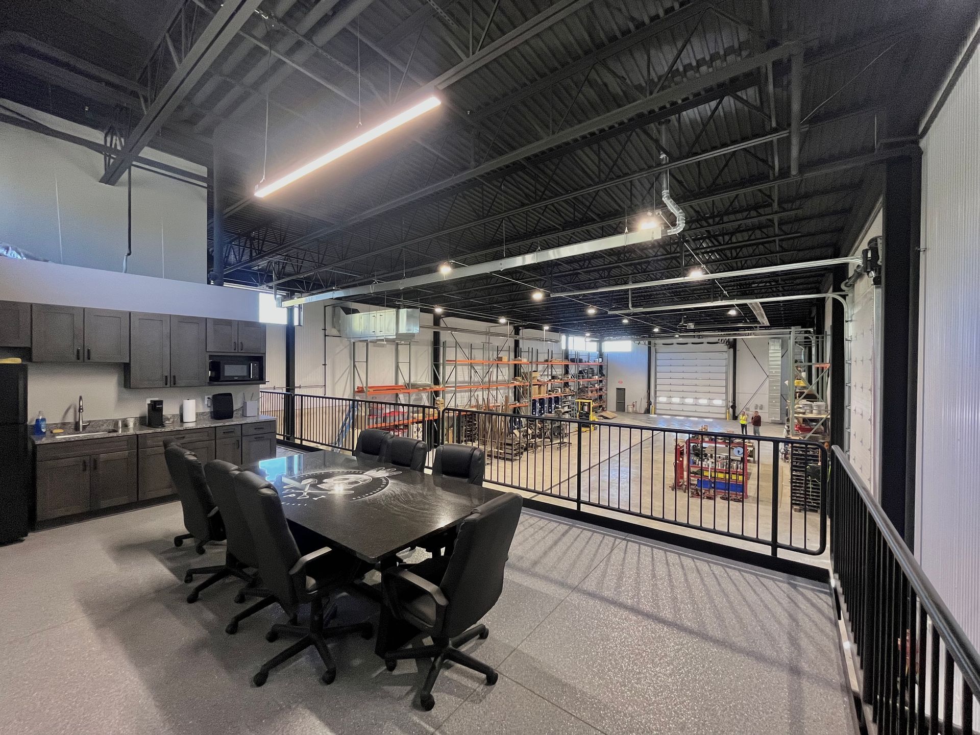 Conference room with view of warehouse. Dark furniture, gray cabinets, open space with metal shelving.