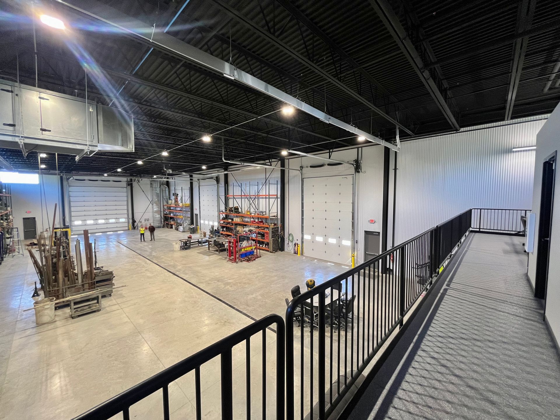 Large industrial warehouse interior with overhead doors, machinery, and a metal walkway.