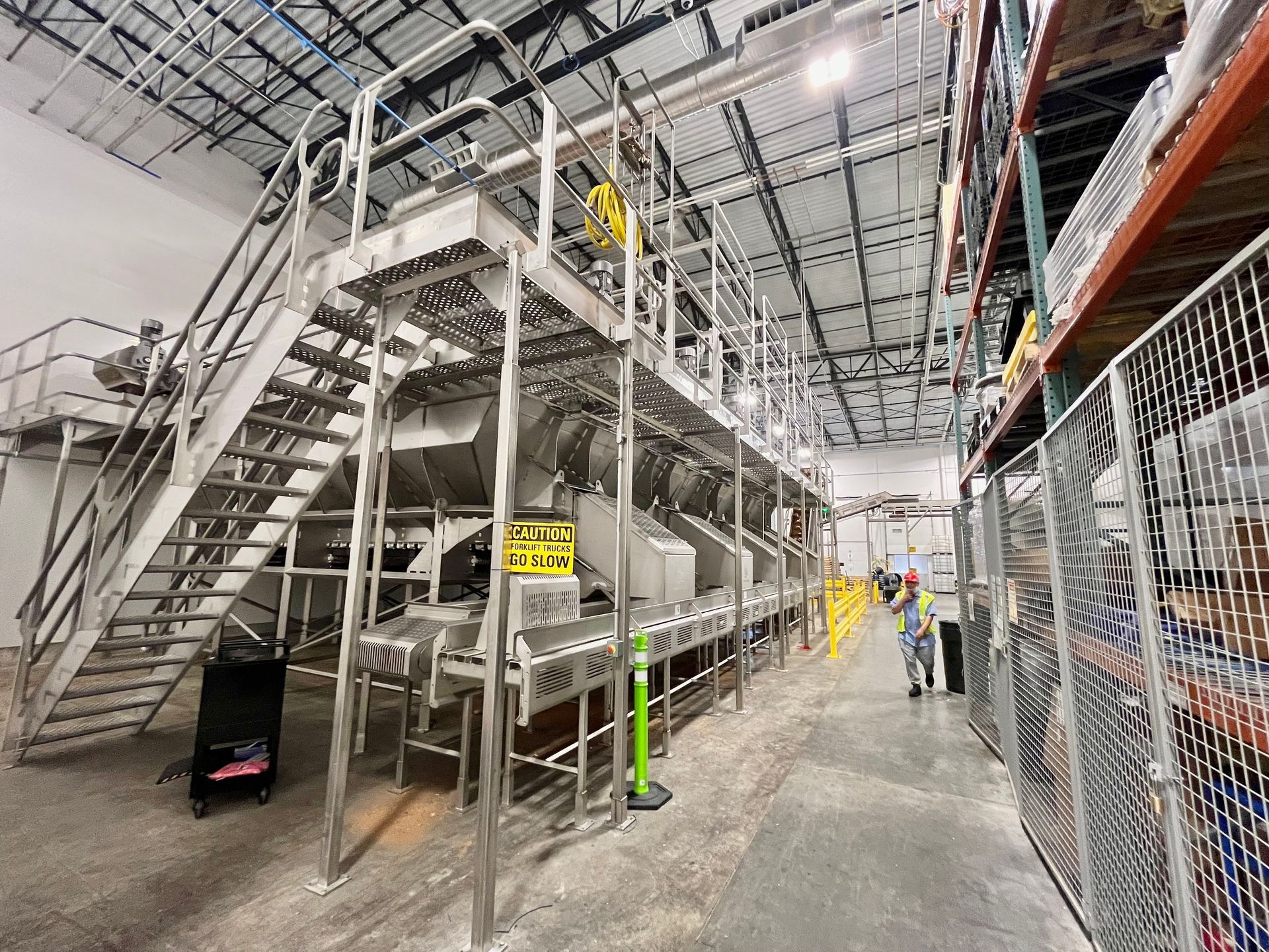 Industrial food processing machinery in a warehouse, with workers and shelving visible.